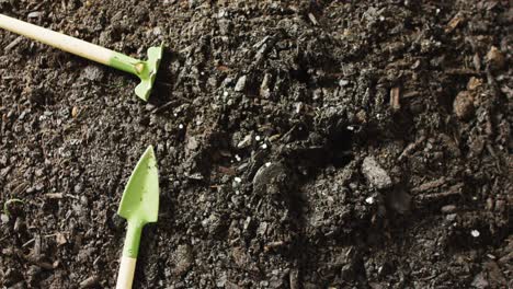 close up video of miniature trowel and rake gardening tools lying on dark soil, with copy space