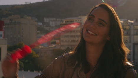 hermosa mujer caucásica soplando burbujas en el techo al atardecer disfrutando de un divertido día de verano con la ciudad en el fondo