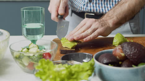 Close-Up-Of-Man-Hands-Slicing-Avocado-And-Cherry-Tomato-To-Prepare-A-Tasty-Toast