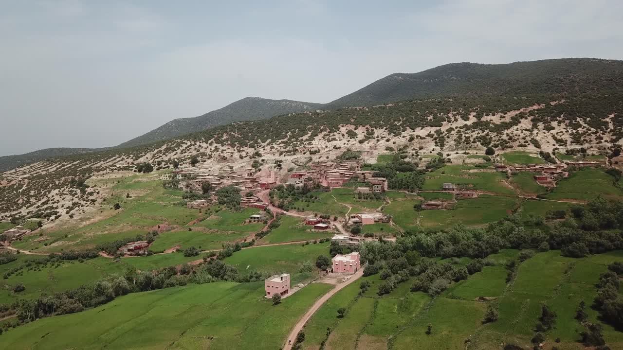 Laaja ilmakuvakulma, joka tallentaa reheviä vihreitä kumpuilevia kukkuloita ja mutkittelevaa hiekkatietä Marokon maaseudulla. Kuvamateriaali korostaa High Atlas -vuoriston seesteistä maalaismaisemaa ja luonnonkauneutta.