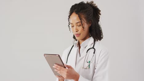 Video-of-biracial-female-doctor-with-stethoscope-using-tablet-on-white-background