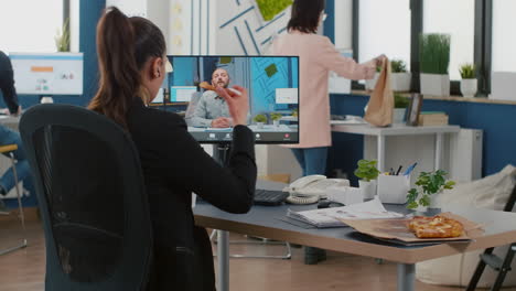 executive manager eating pizza slice discussing with remote collegue during online videocall meeting