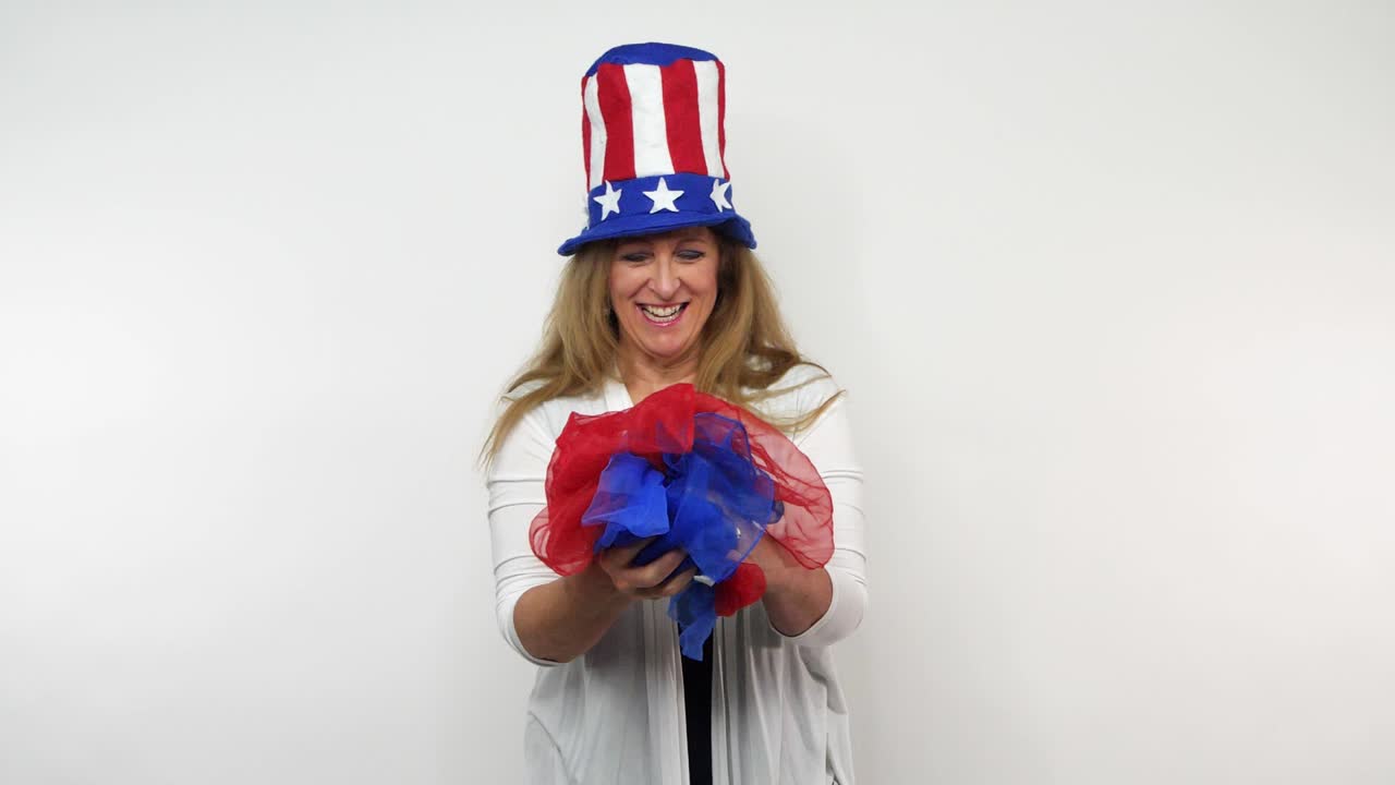 una mujer pelirroja vestida para celebrar a los estados unidos de una manera patriótica sonríe y se ríe con bufandas rojas y azules en las manos