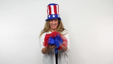 a red haired woman dressed to celebrate the us in a patriotic fashion smiles and laughs with red and blue scarves in her hands