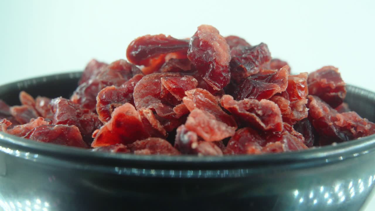 乾燥したクランベリー、赤い果実、360 回転 4 k スローモーションで満たされた回転する黒い光沢のある皿、クローズ アップ