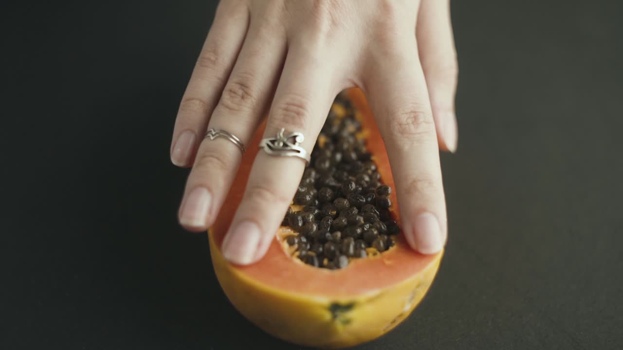 Close up of woman's hand gently touching a papaya cut in half, moving with her fingers from back to front