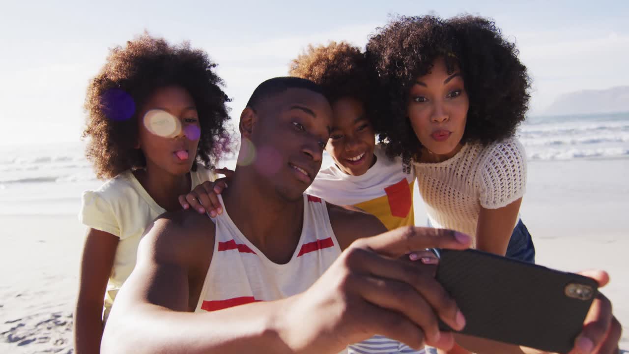 padres afroamericanos y sus hijos toman una selfie con un teléfono inteligente en la playa
