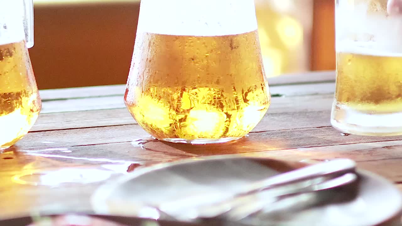 Close-up of hands clinking glasses filled with drinks on a sunlit wooden table.