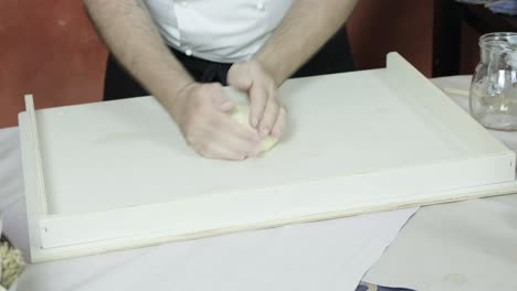 chef rolls and forms dough ball on floured wooden prep surface shaping with hands