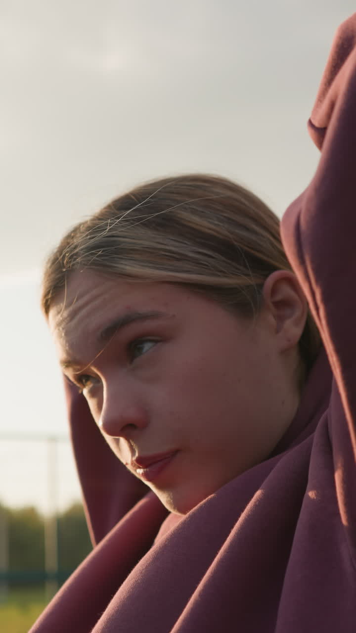 Side view of woman tying hair backward outdoors, sunlight creating a glowing effect around her hand, soft sunlight highlights her features as she prepares for outdoor activities in a natural setting