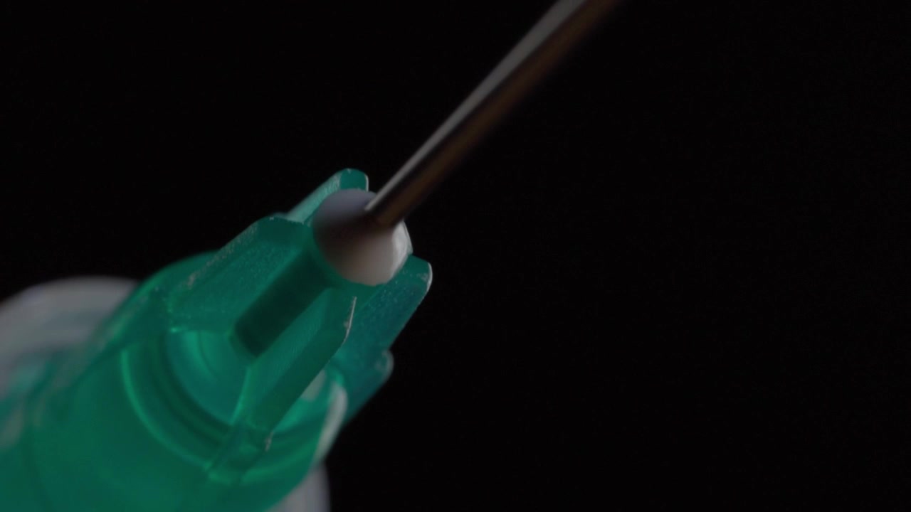 Macro close up of medical syringe with needle attached, focusing on the transparent green plastic hub and metal needle against a dark background