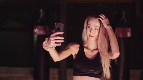 Atleta-Femenina-Ajustando-El-Cabello-Mientras-Toma-Selfie-A-Través-Del-Teléfono-Inteligente-En-El-Gimnasio