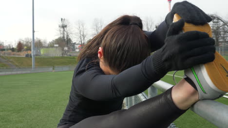 sporty brunette stretching leg and foot on track railing, outdoor day