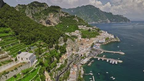 Amalfi-Italy-Aerial-v8-cinematic-fly-along-rocky-cliff-towards-Mediterranean-coastal-town-capturing-terraced-hillsides,-waterfront-harbor-and-pristine-sea-views---Shot-with-Mavic-3-Cine---May-2023