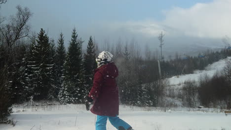 child throws snow ball into white field at as flakes fall, over the shoulder