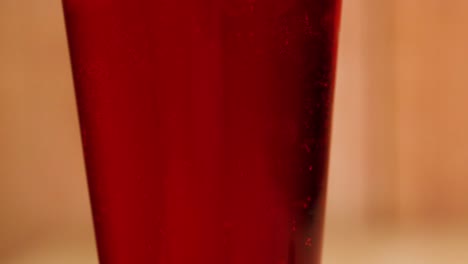 a detailed view of red liquid inside a transparent glass against a blurred background.