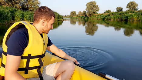 man in life vest on inflatable boat touching river water