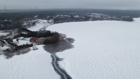 Retirada-Aérea-Se-Retira-Sobre-El-Lago-Cubierto-De-Nieve-Del-Invierno-Cerca-De-Suwalki-Gap,-Ciudad-Rural-Masuria-En-La-Distancia