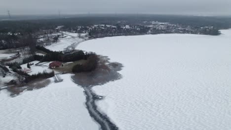 aerial pullback retreats above winter snow covered lake near suwalki gap, rural town masuria in distance