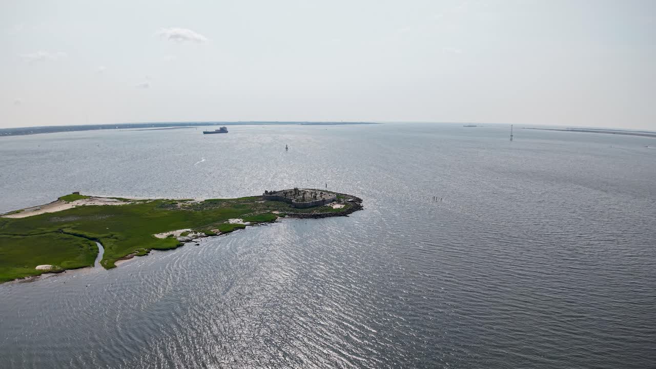 Drone aerial footage capturing a solitary patch of green land surrounded by expansive blue water and distant boat near Charleston harbor, South Carolina