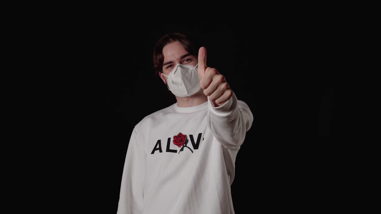 Trendy Young Man wearing facemask giving thumbs up, wide, black background
