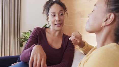 happy biracial lesbian couple relaxing on couch together, holding hands and talking, in slow motion