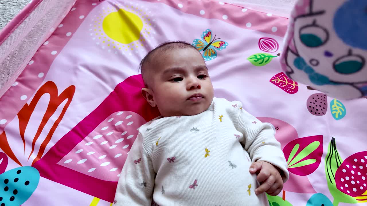 Three month old baby girl lying on a pink play mat with colorful flowers and butterflies. dolly, slow motion