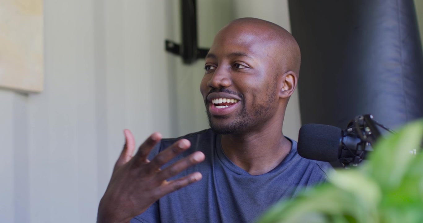 Adult African American man laughing and gesturing after off-frame question during podcast with mic