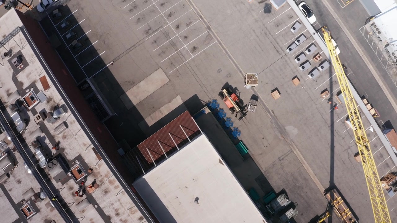 Bird's eye aerial shot following a construction crane hoisting an old HVAC unit during renovation work in Baldwin Park, California. 4K