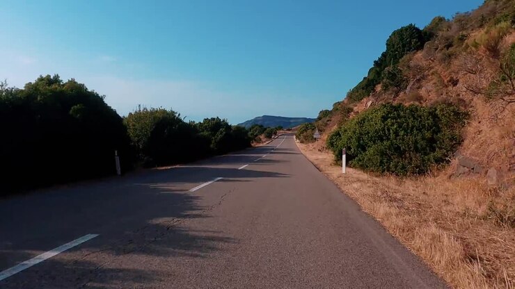 Strada asfaltata vuota che curva lungo la vegetazione secca e le colline che conducono verso il mare blu e l'orizzonte celeste in una giornata di sole nella pittoresca zona costiera di Creta, Grecia
