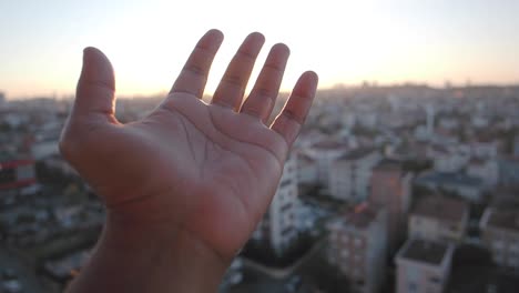 hand reaches towards the city sunset
