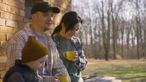 Camera-zoom-out-of-caucasian-couple-talking-with-her-son-while-they-drinking-tea-outside-a-country-house