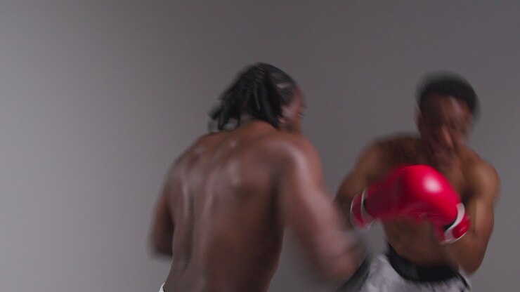 Scatto in studio di azione in tempo reale di due pugili maschi che indossano i guantoni e combattono in un incontro di boxe su sfondo grigio 1