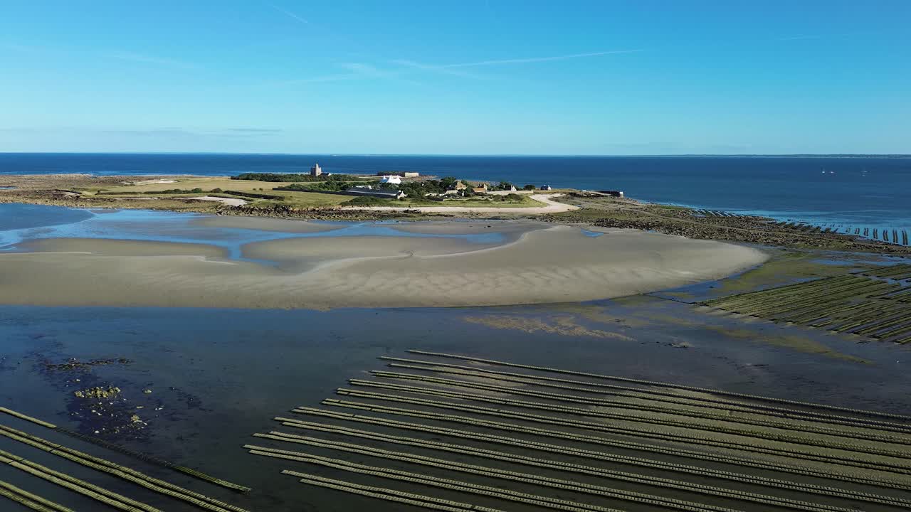 Aerial drone footage of Tatihou Island in Normandy on a sunny day, revealing its historic fort, green landscapes, and the vast oyster beds stretching across the glistening tidal flats