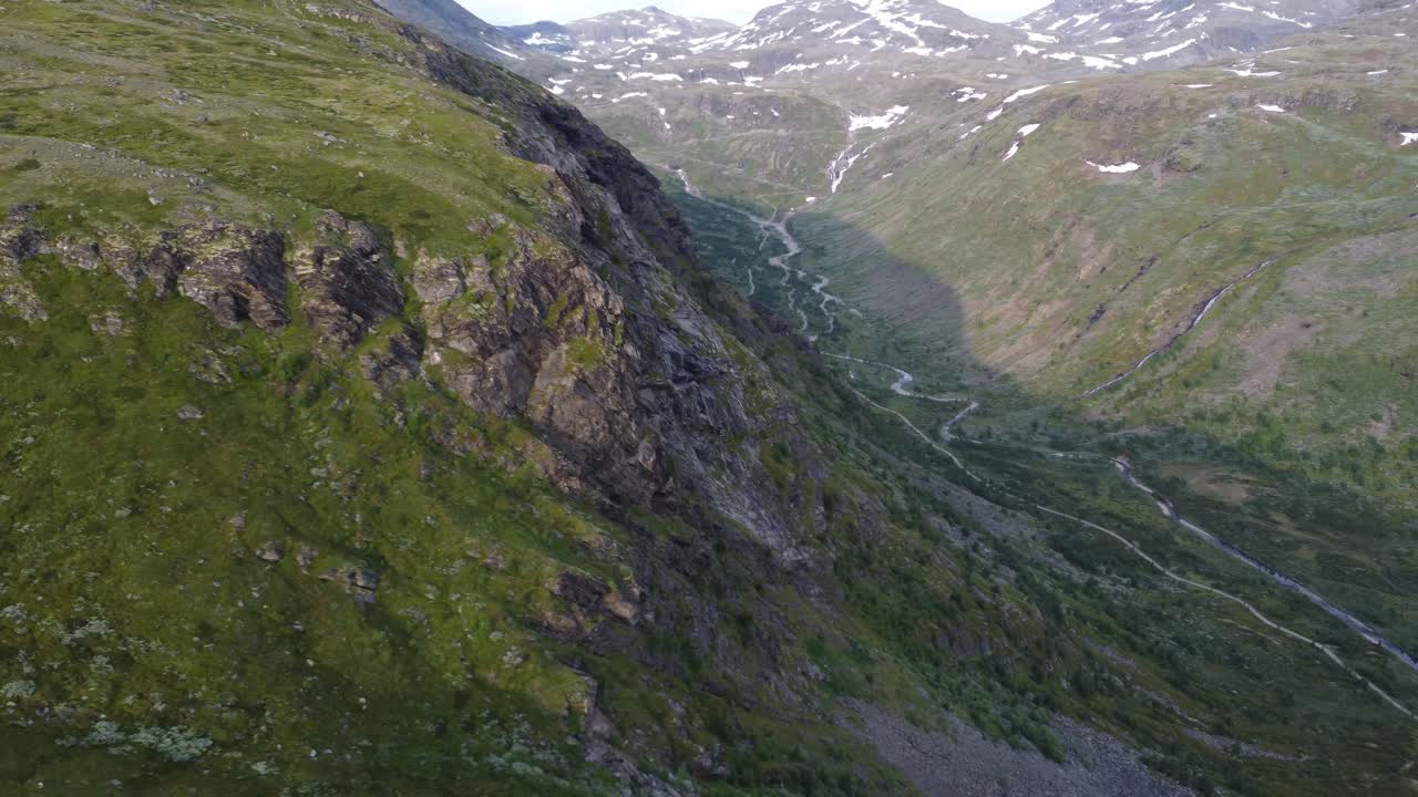 Câmera passa pela encosta de uma montanha e revela a longa estrada solitária estendida atrás dela