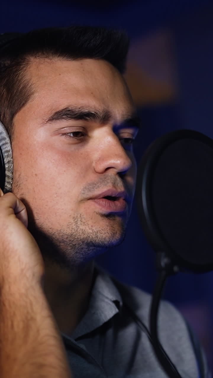 Emotional male singer performing a song in the dark studio. Song recording in the modern professional sound studio. Vertical video