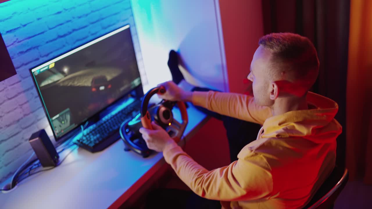 Man paying car simulator. Handsome man playing with steering wheel in video game at home