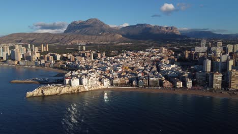 Cinematic-4K-aerial-shot-of-Benidorm-touristic-beachfront-destination-with-mountains-in-background-at-sunset