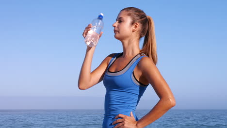 Mujer-En-Forma-Bebiendo-Agua-En-La-Playa