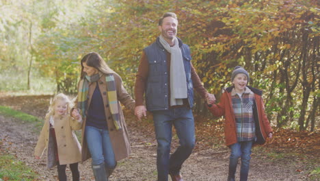 familia con padres maduros y dos niños tomados de la mano caminando por la pista en el campo de otoño