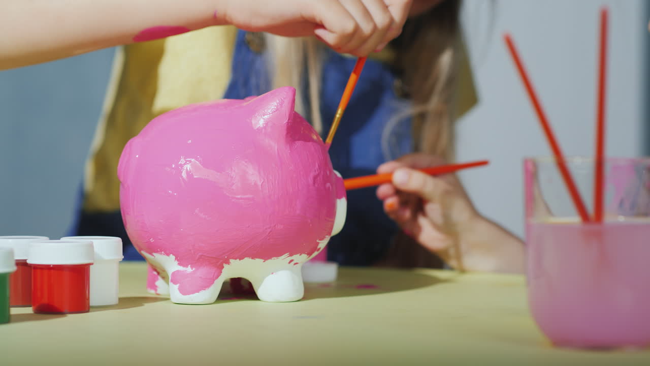 los niños pintan la alcancía con pintura rosa en el marco solo se ven las manos