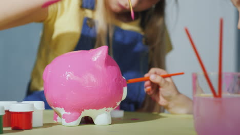 children paint the piggy bank with pink paint in the frame are visible only hands