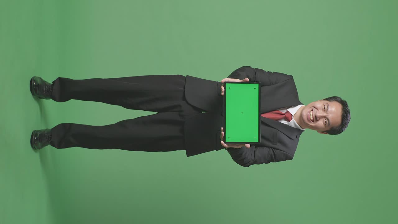 cuerpo lleno de hombre de negocios asiático mostrando pantalla verde de la tableta en el fondo de la pantalla verde en el estudio
