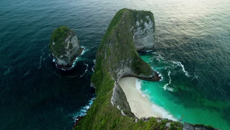 the iconic t rex shaped cliff of kelingking beach is captured in aerial footage during golden hour with brilliant blue ocean and golden hues lighting the dramatic coast of nusa penida.