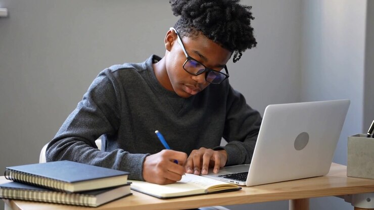 Putting blue pen on spiral notebook, teenage student writing at study nook studying with laptop