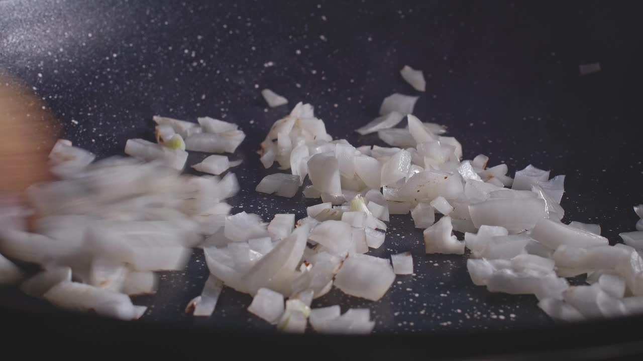 Mixing chopped onion in a frying pan using a wooden spoon, close up view