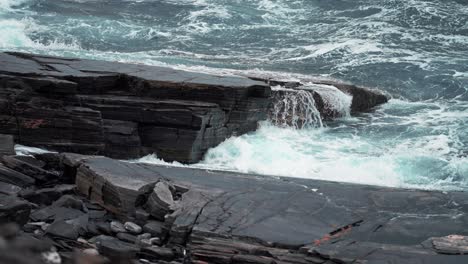 heavy waves hit the dark rocks on the shoreline