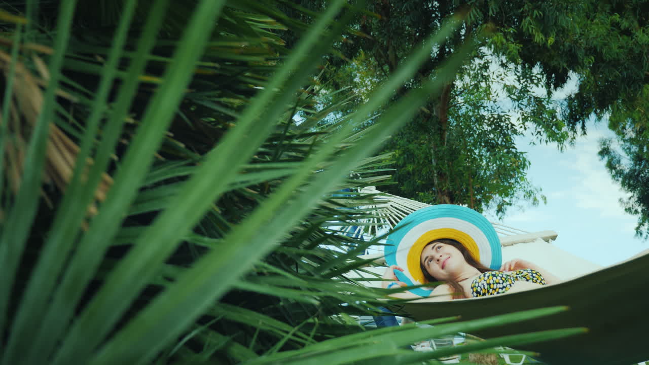 lejos de la civilización, una joven se relaja en una hamaca alrededor de las palmeras verdes, el cielo azul