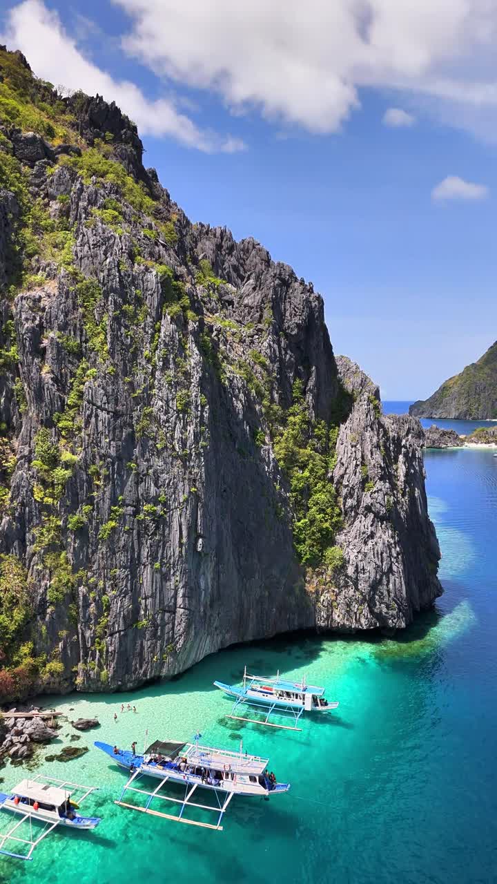 Drone melayang di atas Pantai Talisay, beberapa perahu di perairan biru kehijauan dan langit biru di Palawan, Filipina