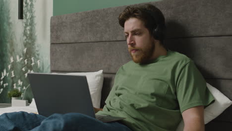 el niño está viendo videos en una computadora portátil y usando un teléfono inteligente mientras come palomitas de maíz en la cama en el dormitorio